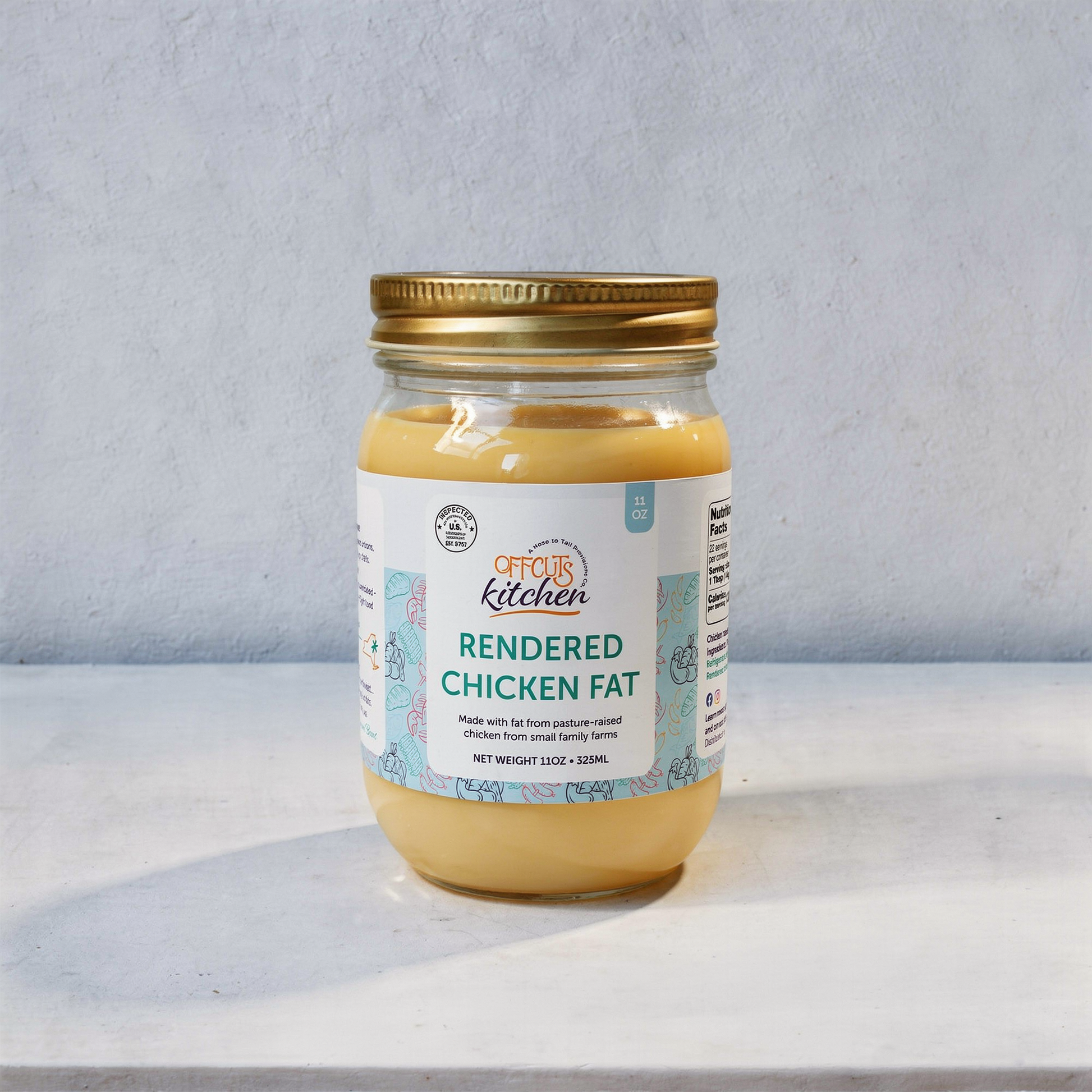 Jar of rendered chicken fat with a gold lid on a light gray background