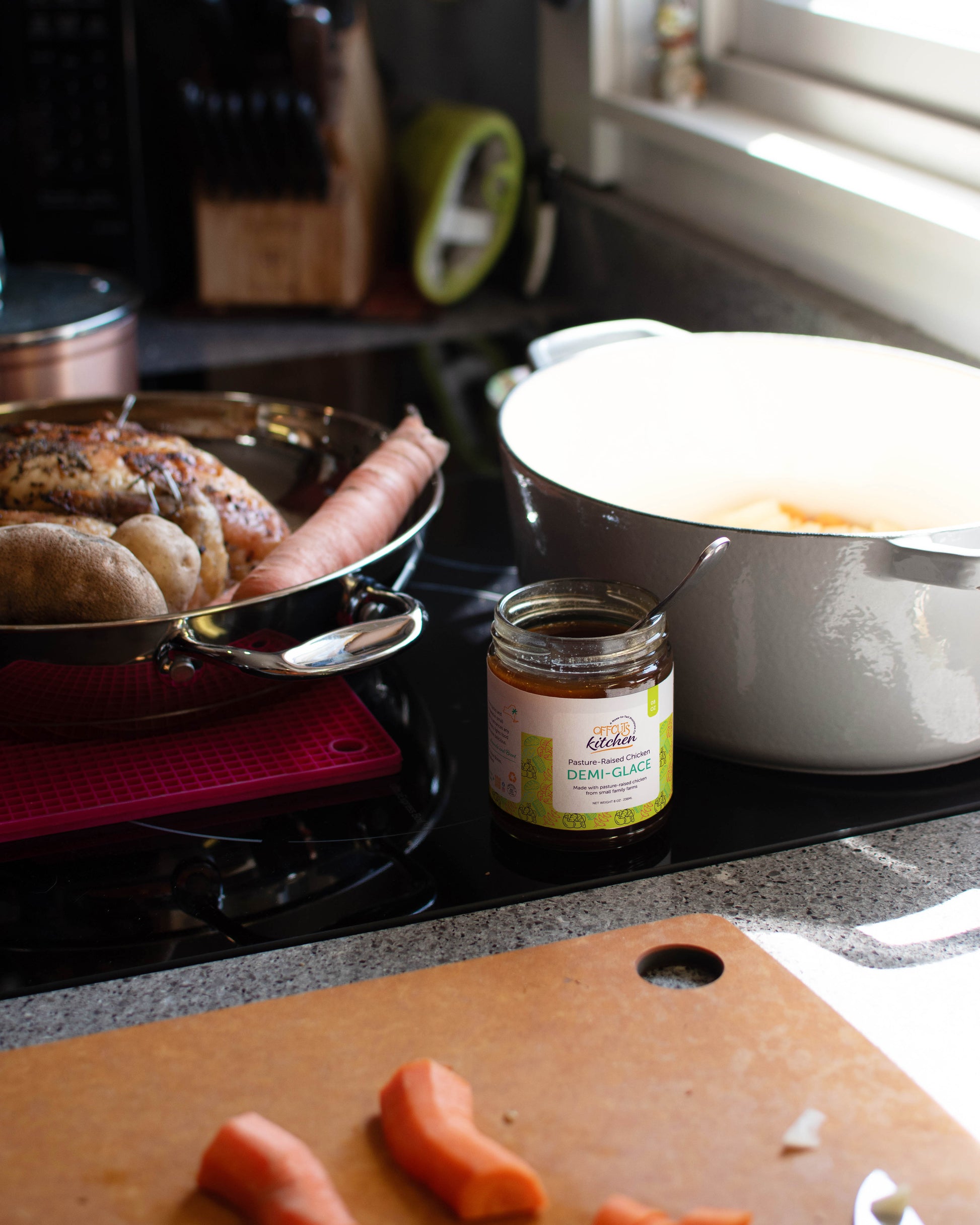 Stove top with pan of food, jar of jam, and cutting board with carrots in a kitchen setting.