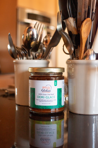 Jar of demi-glace sauce on a kitchen counter with utensils in the background